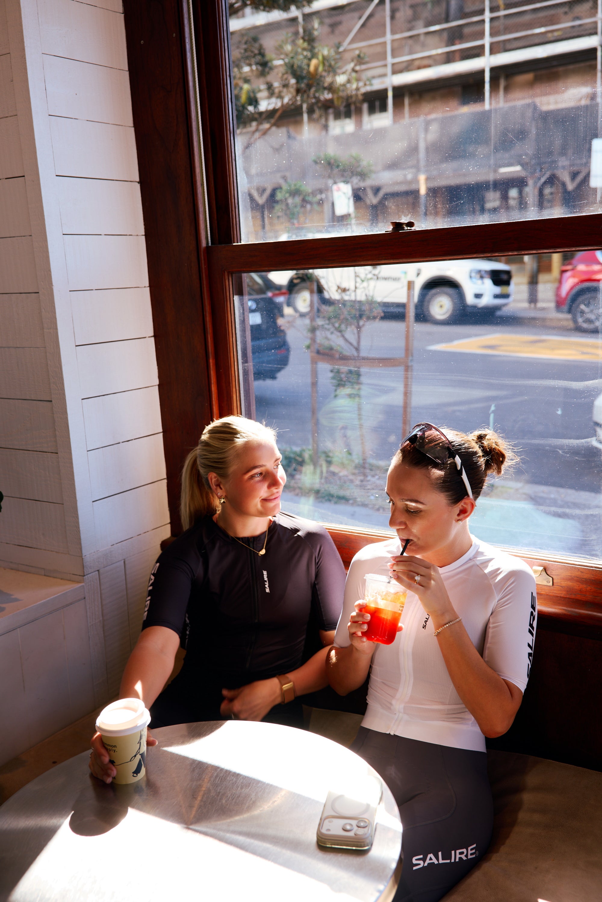 Two cyclists wearing Salire kits sitting at a table in a cafe