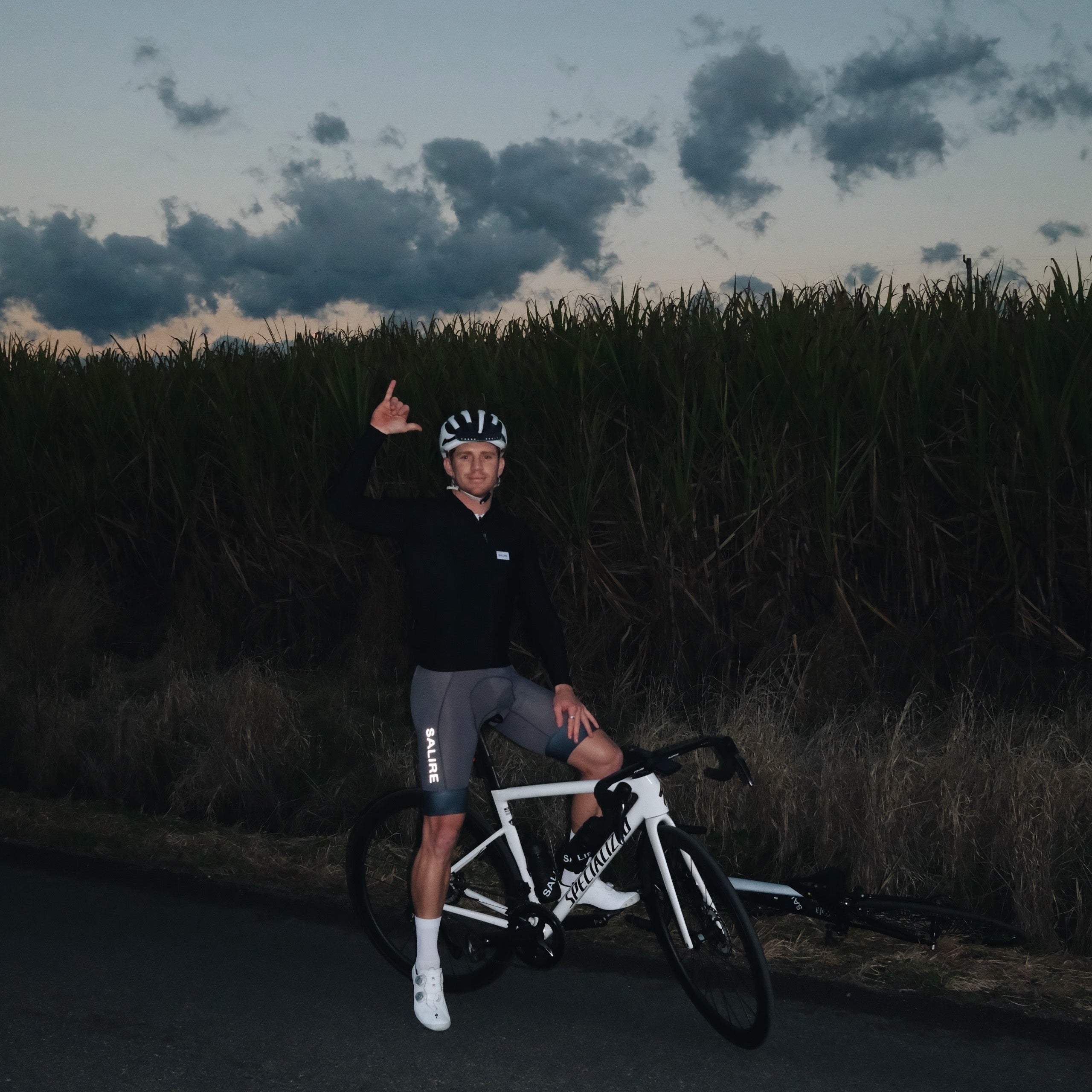 Cyclist giving a thumbs-up sign with a bicycle on a road at dusk.